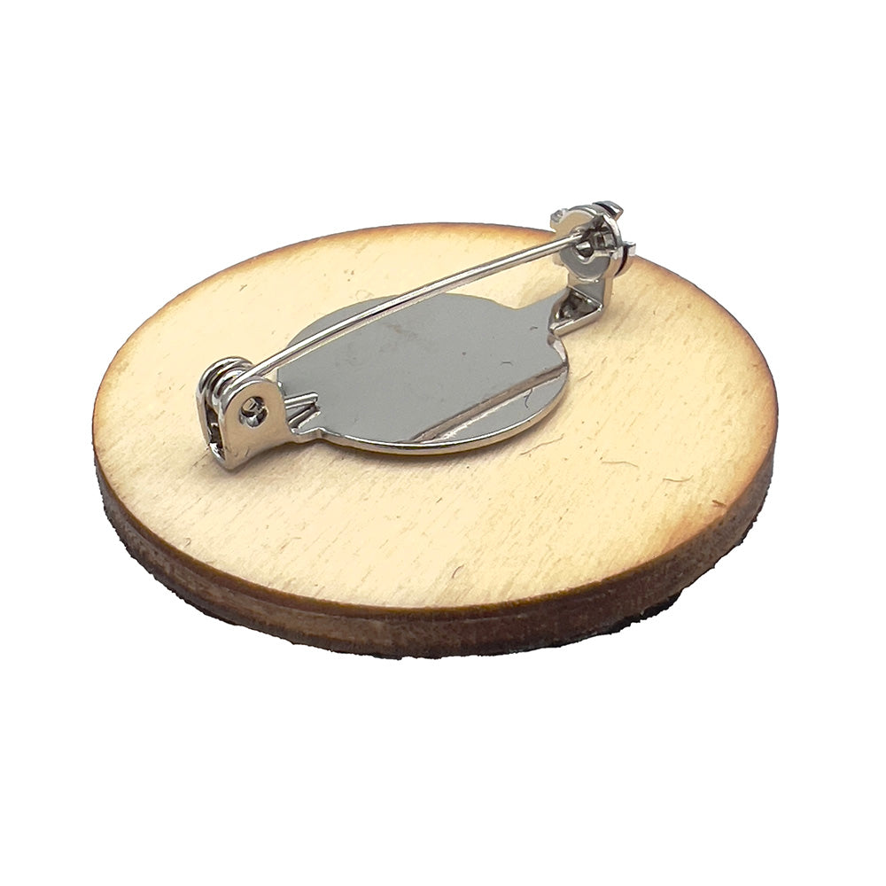 Back view of a wooden badge with a metal pin fastening, designed by The Unruly Stitch, showing an angled perspective.
