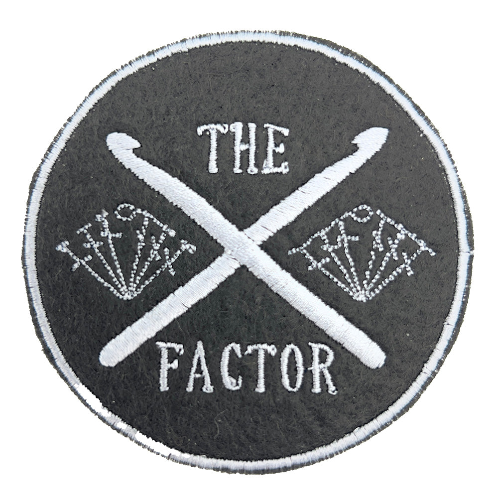 Close up of embroidered felt patch featuring crossed crochet hooks with stitch symbols.