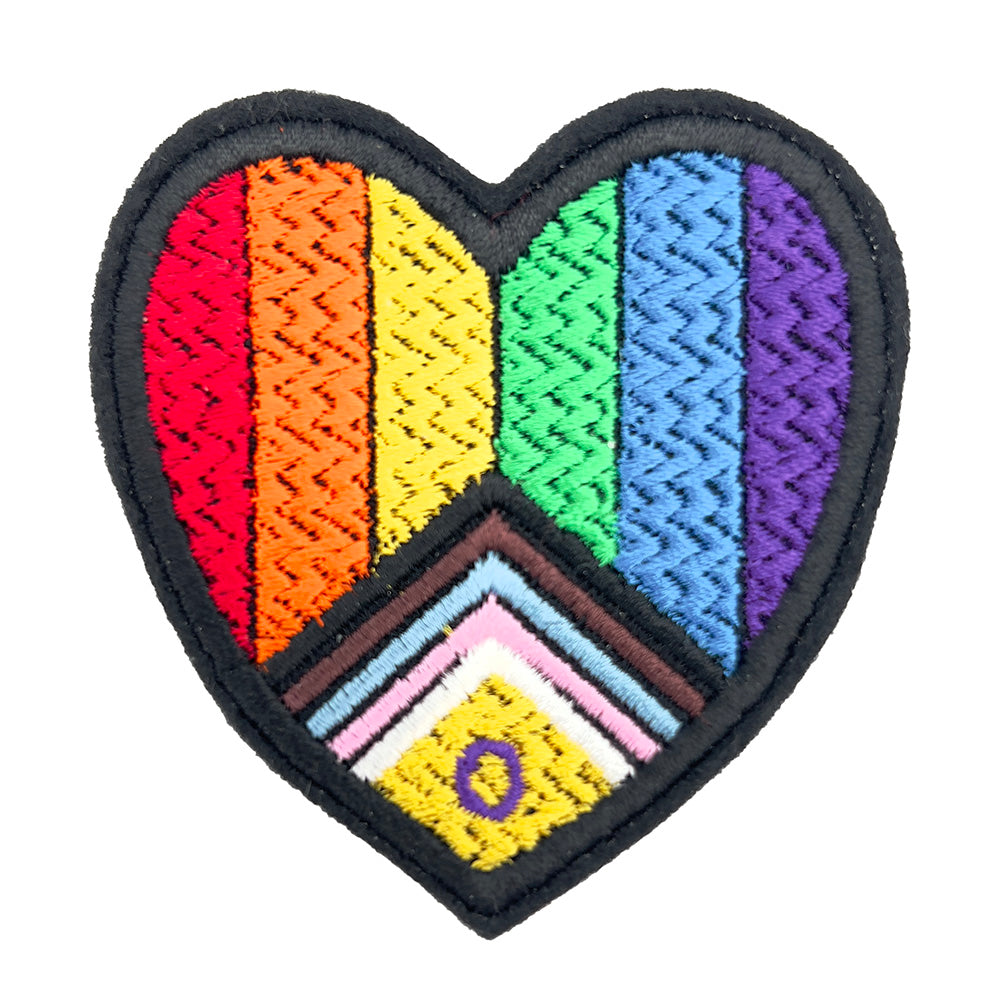Close-up view of a heart-shaped embroidered patch featuring the Inclusive Intersex Pride flag design, with red, orange, yellow, green, blue, purple, black, and brown stripes, and a triangle with pink, white, and blue stripes, and a yellow triangle with a purple circle.