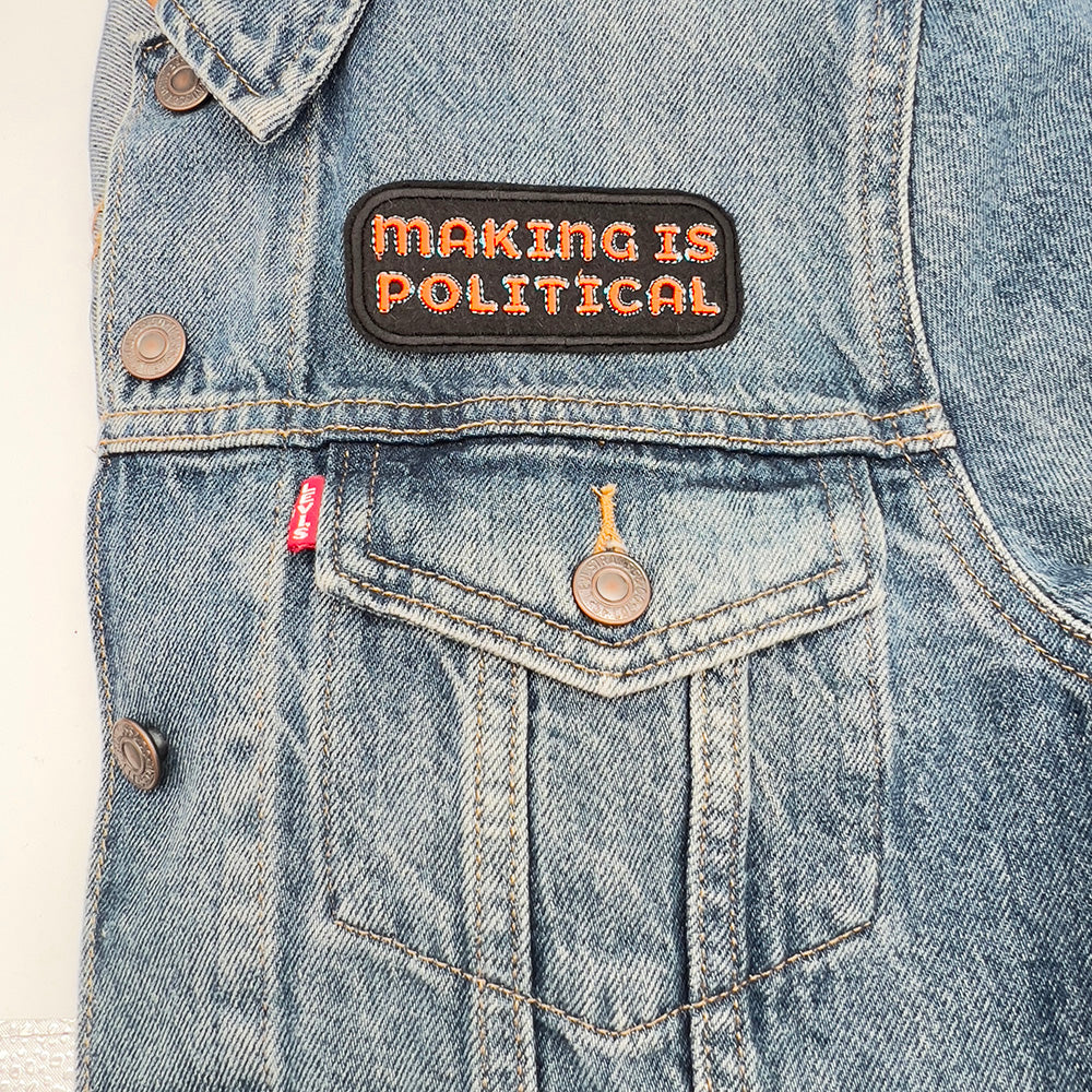 Patch on denim jacket: The "Making is Political" embroidered felt patch ironed onto the chest pocket of a denim jacket, displaying how the patch looks when attached to clothing.
