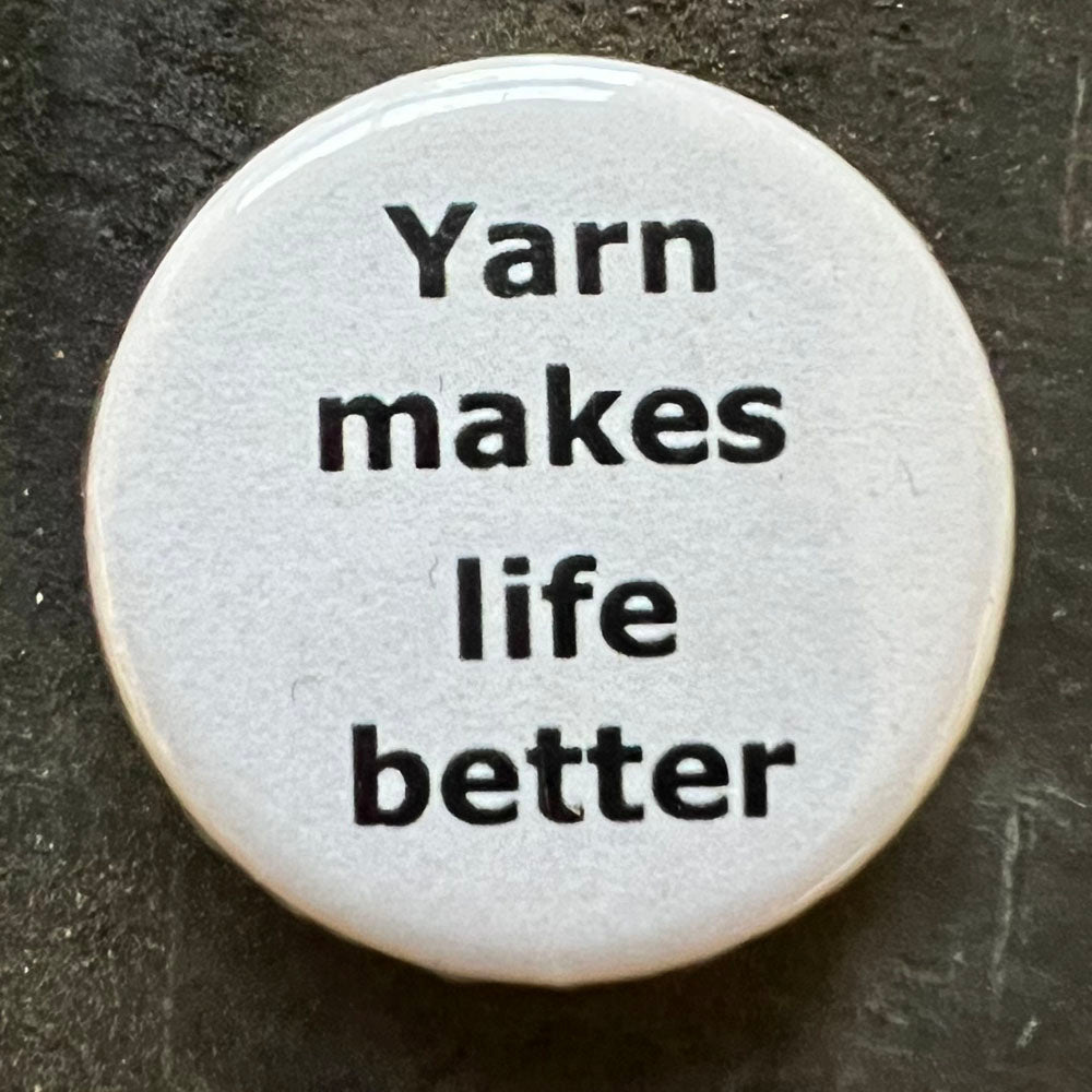 Close-up of a white Yarn makes life better pin badge with black text.