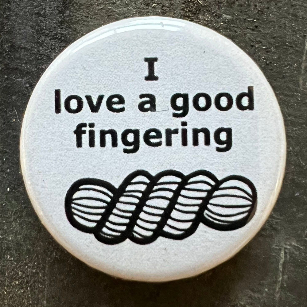 Close-up of a white I love a good fingering pin badge with black text.