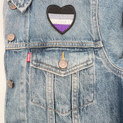 Asexual Pride flag heart-shaped embroidered felt patch attached to the front pocket of a blue denim jacket from The Unruly Stitch.