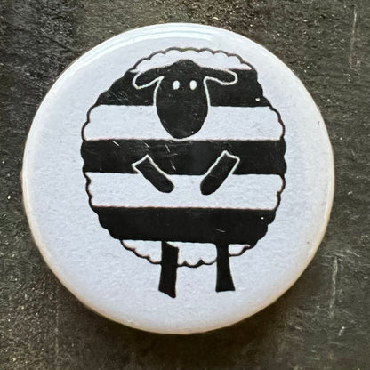 Close-up of a white pin badge with a black and white sheep design, featuring the sheep with horizontal black stripes.