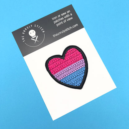 Bisexual pride flag heart-shaped embroidered felt patch displayed on a branded card with "The Unruly Stitch" logo. The patch features horizontal stripes in pink, purple, and blue.