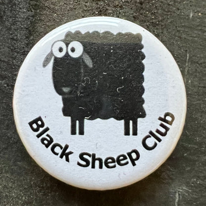 Close-up of a white pin badge with a black sheep design and the text "Black Sheep Club" in black letters.