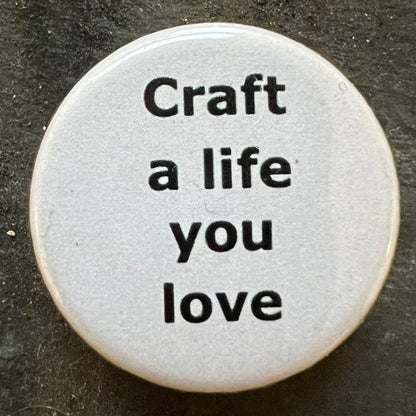 Close-up of a white Craft a life you love pin badge with black text.
