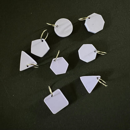 A set of geometric stitch markers in violet perspex on jump rings, including circles, triangles, squares, pentagons, hexagons, and octagons, displayed on a black background.