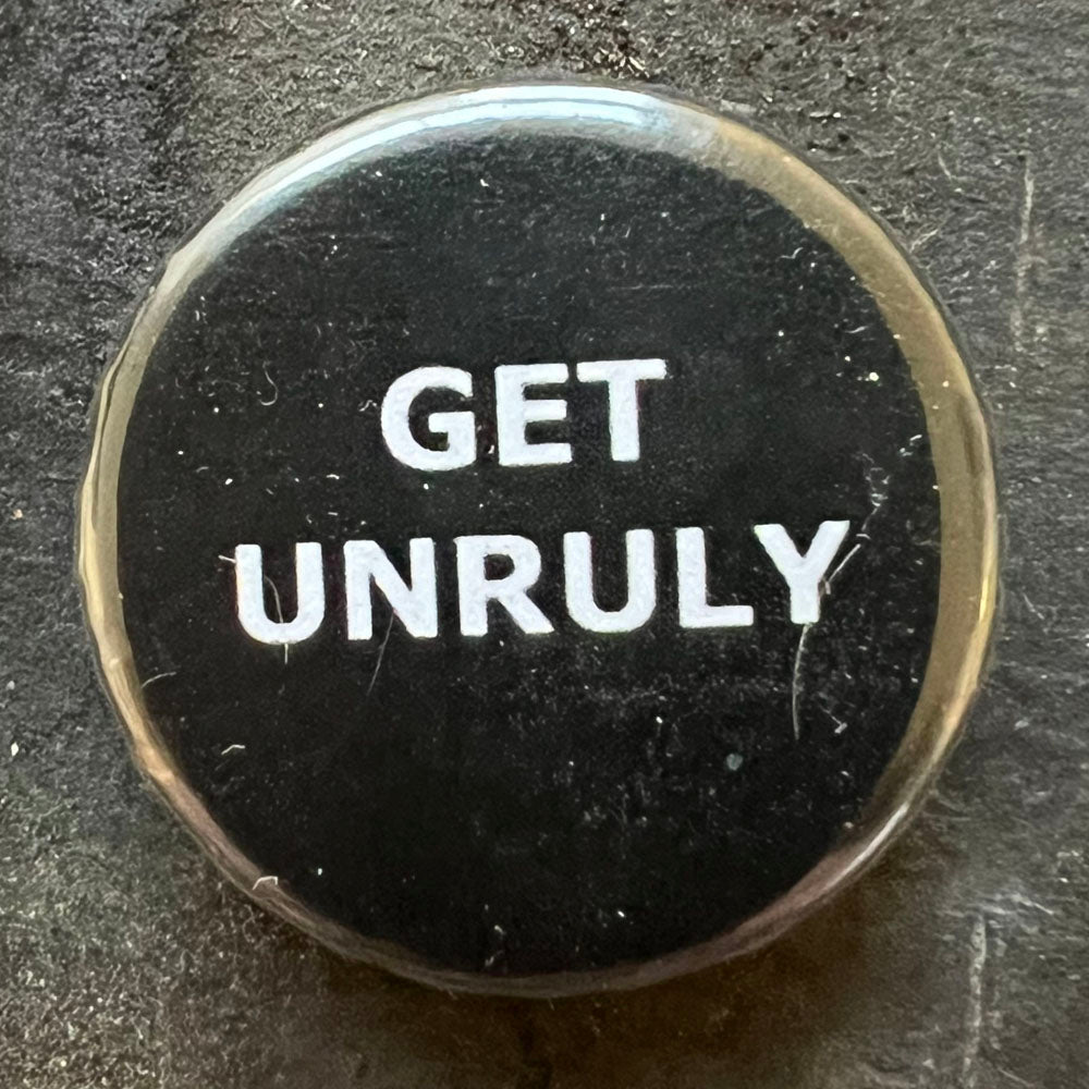 Close of of black pin badge with white text "GET UNRULY"