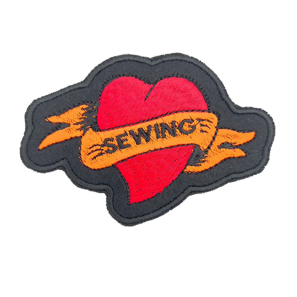 Close-up image: Close-up view of an embroidered felt patch shaped like a heart with a banner. The patch features a red heart with an orange banner that reads "SEWING," with black outlines and details.
