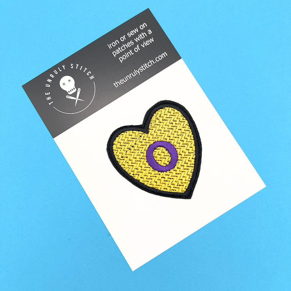 Heart-shaped Intersex Pride flag embroidered patch displayed on a branded card from The Unruly Stitch, against a blue background.