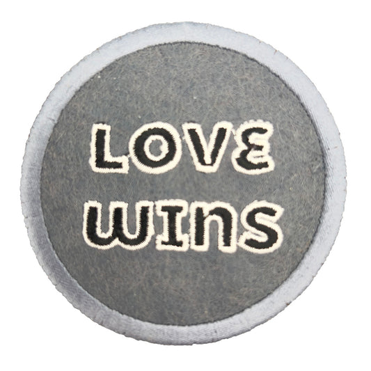 A close-up image of a round embroidered felt patch with the text "LOVE WINS" in white letters, set against a black background with a gray border.