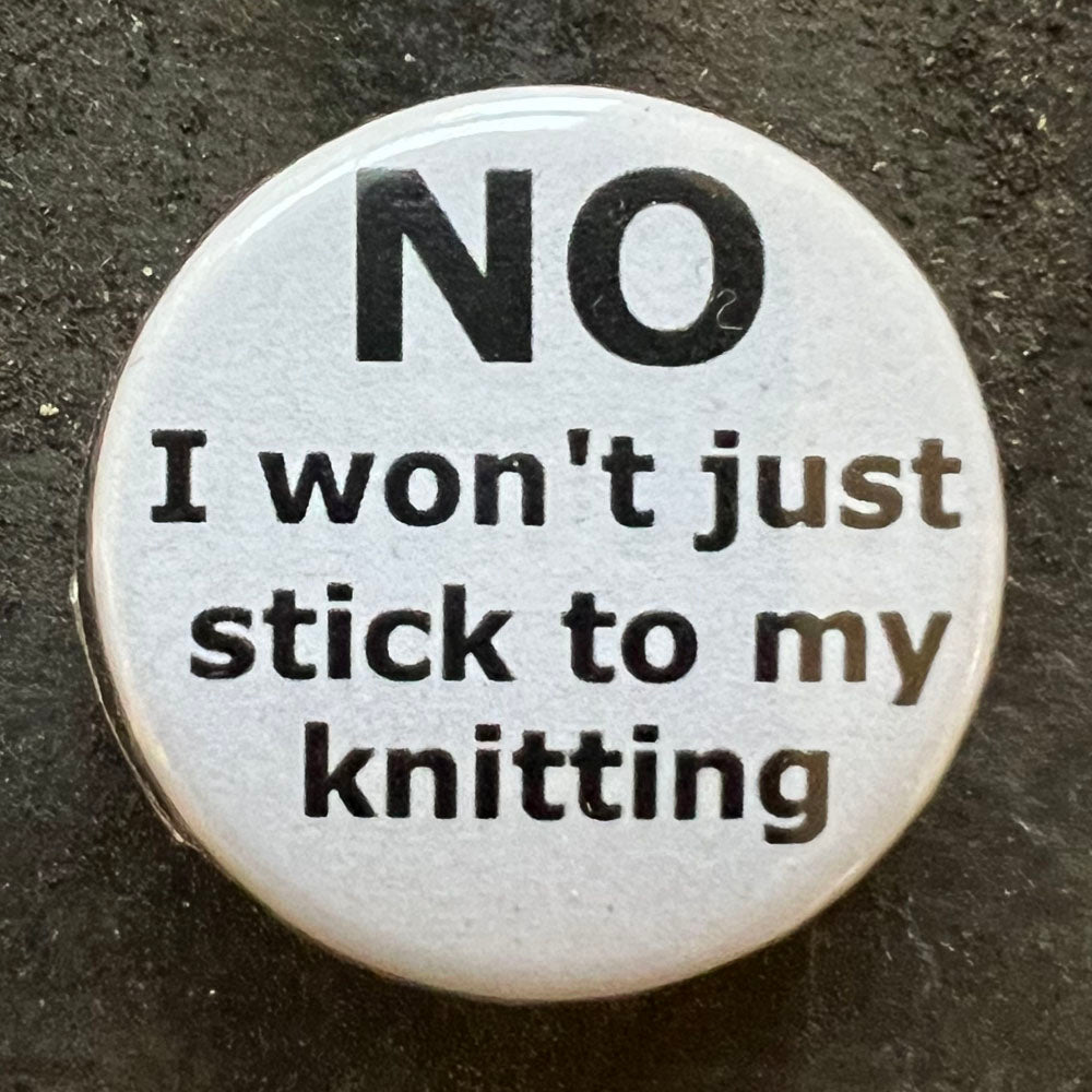 Close-up of a white NO I won't stick to my knitting pin badge with black text.