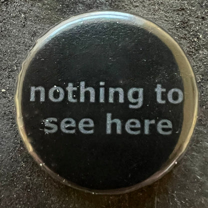 Close-up of a black pin badge with grey text 2nothing to see here"