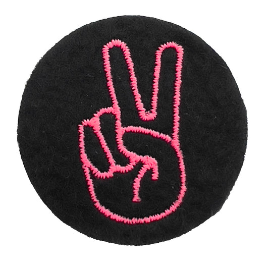 Close-up of a felt badge with an embroidered peace or victory hand sign in pink threads on a black background, designed by The Unruly Stitch.