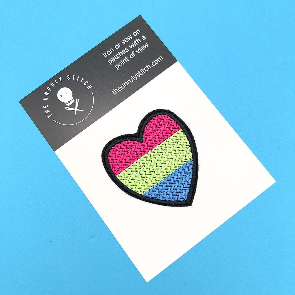 Heart-shaped polysexual pride flag patch on a white card with "The Unruly Stitch" branding, set against a blue background.