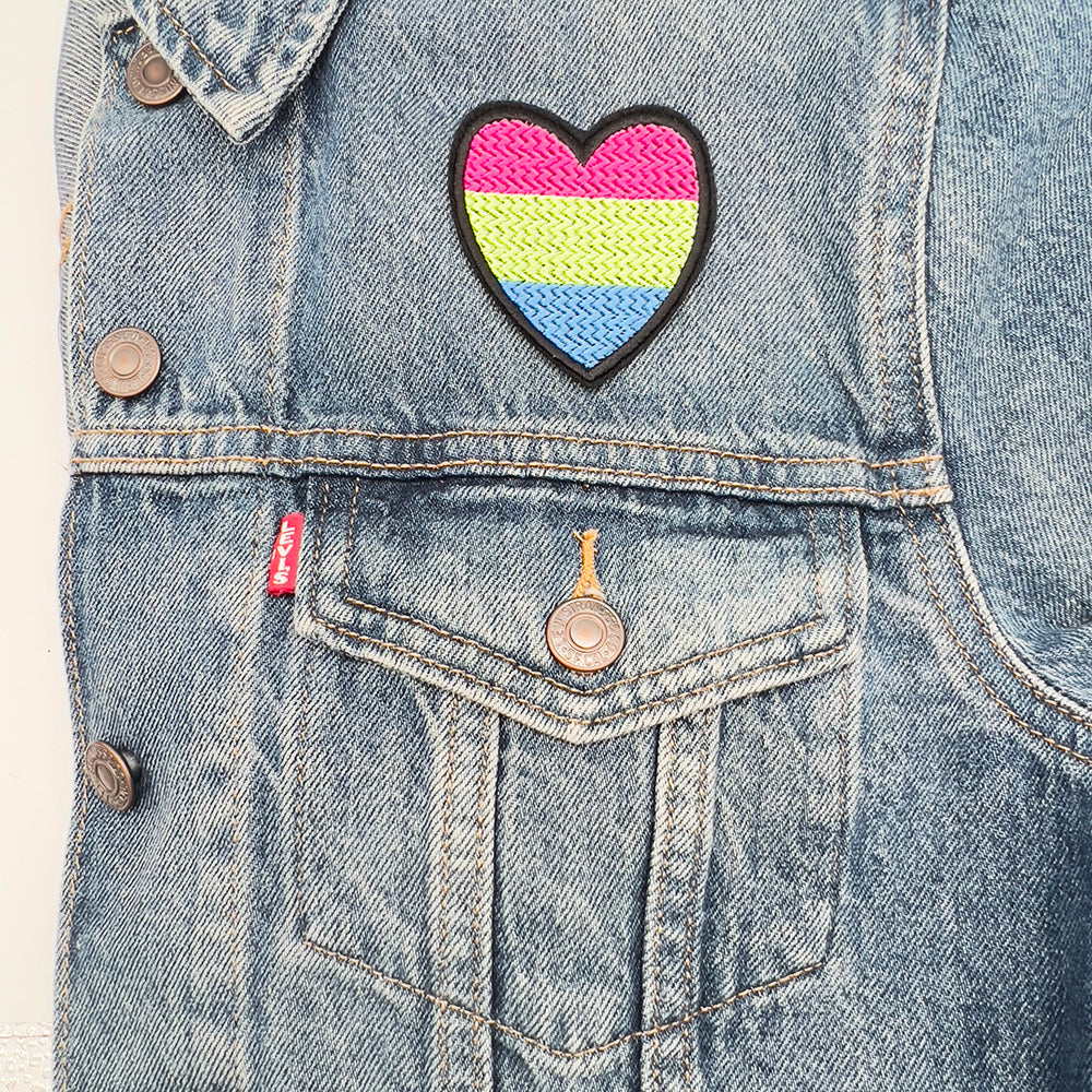 Heart-shaped polysexual pride flag patch ironed onto a denim jacket above the left-side pocket.