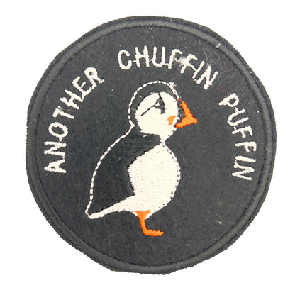 A circular embroidered felt patch with a black background, featuring a puffin with an orange beak and feet, white belly, and black and white head. Above the puffin, the text reads "ANOTHER CHUFFIN PUFFIN" in white stitching.
