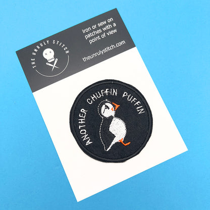 A circular embroidered felt patch with a puffin design and the text "ANOTHER CHUFFIN PUFFIN" in white stitching, attached to a white card. The card has a blue background and includes branding details for "The Unruly Stitch."