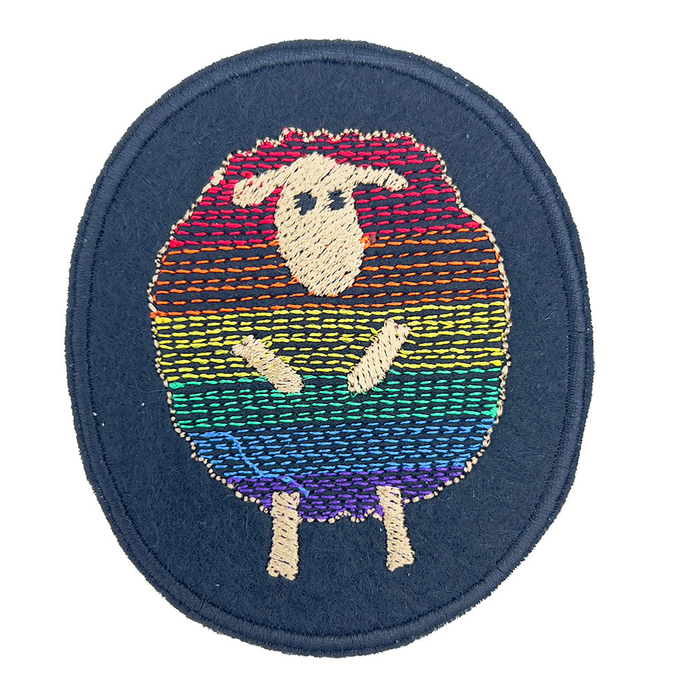 Close-up of a round felt patch with a design of a sheep. The sheep's body is filled with horizontal rainbow stripes, representing the colors of the pride flag. The sheep is outlined in beige, with a beige face, ears, and legs. The background of the patch is black.