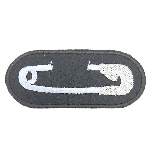 Close-up Image: Close-up view of an embroidered felt patch depicting a white safety pin on a black background. The pin is detailed in silver grey thread with precise stitching.