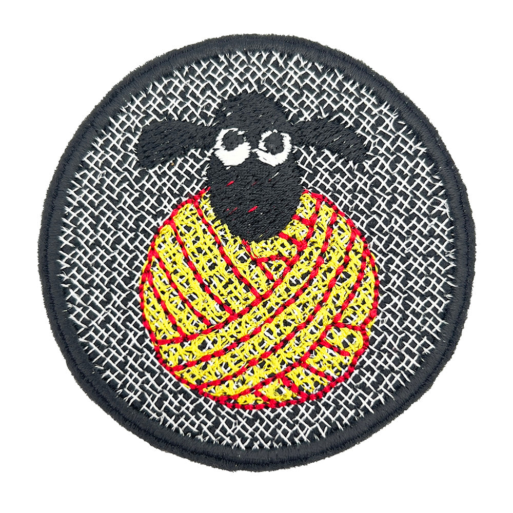 A close-up of an embroidered felt patch featuring a black sheep's head with white eyes, positioned on top of a ball of yellow and red yarn, all set against a black background with white cross-stitch details.