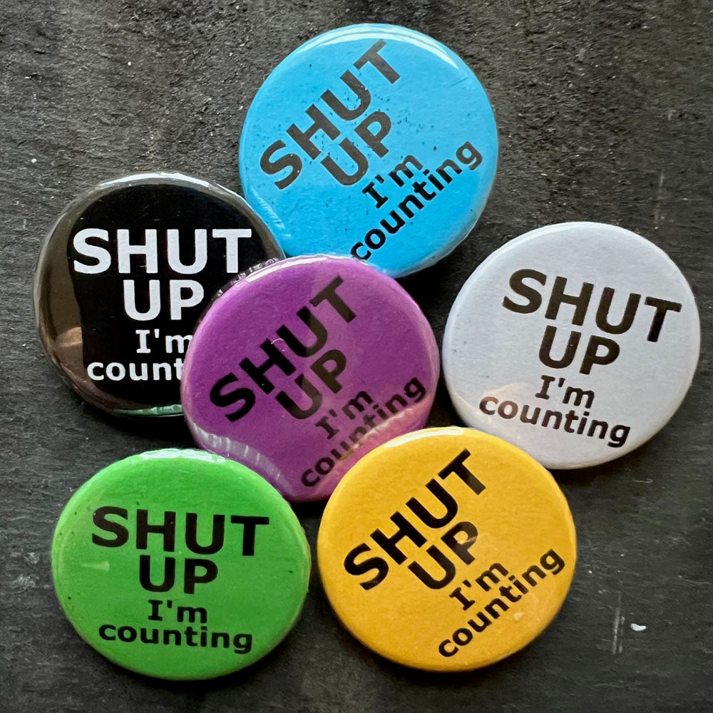 Six SHUT UP I'm counting pin badges in black, blue, pink, green, yellow, and white.