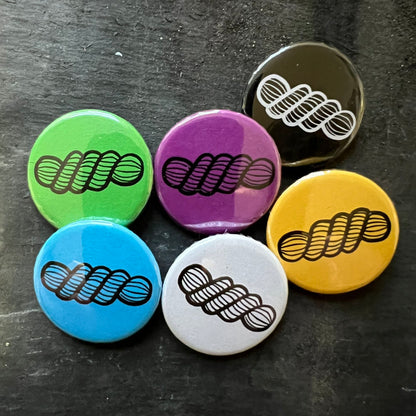 Set of colorful pin badges featuring a skein of yarn design in black, blue, green, purple, yellow, and white.