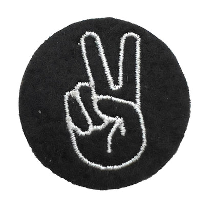 Close-up of a felt badge with an embroidered peace or victory hand sign in white threads on a black background, designed by The Unruly Stitch.