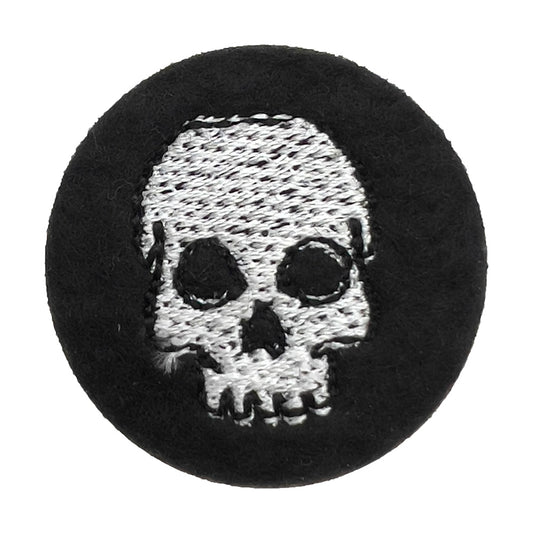 Close-up of a black felt badge featuring a white embroidered skull. The badge is circular and the skull design is centered with detailed stitching.