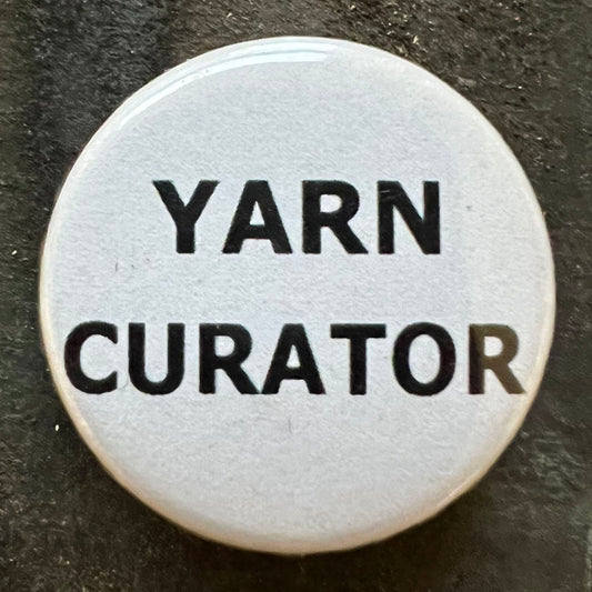Close-up of a white YARN CURATOR pin badge with black text.