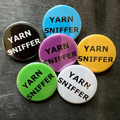 Six Yarn Sniffer pin badges in black, blue, pink, green, yellow, and white.