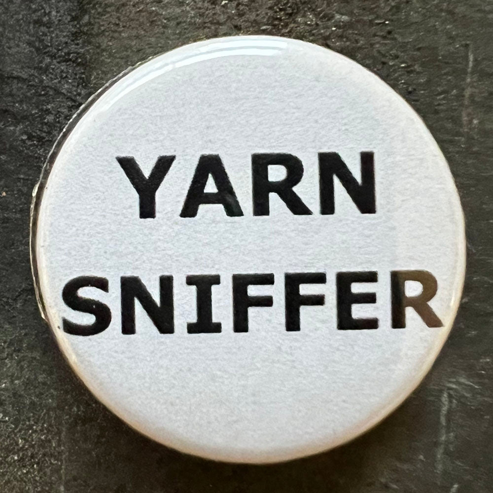 Close-up of a white Yarn Sniffer pin badge with black text.