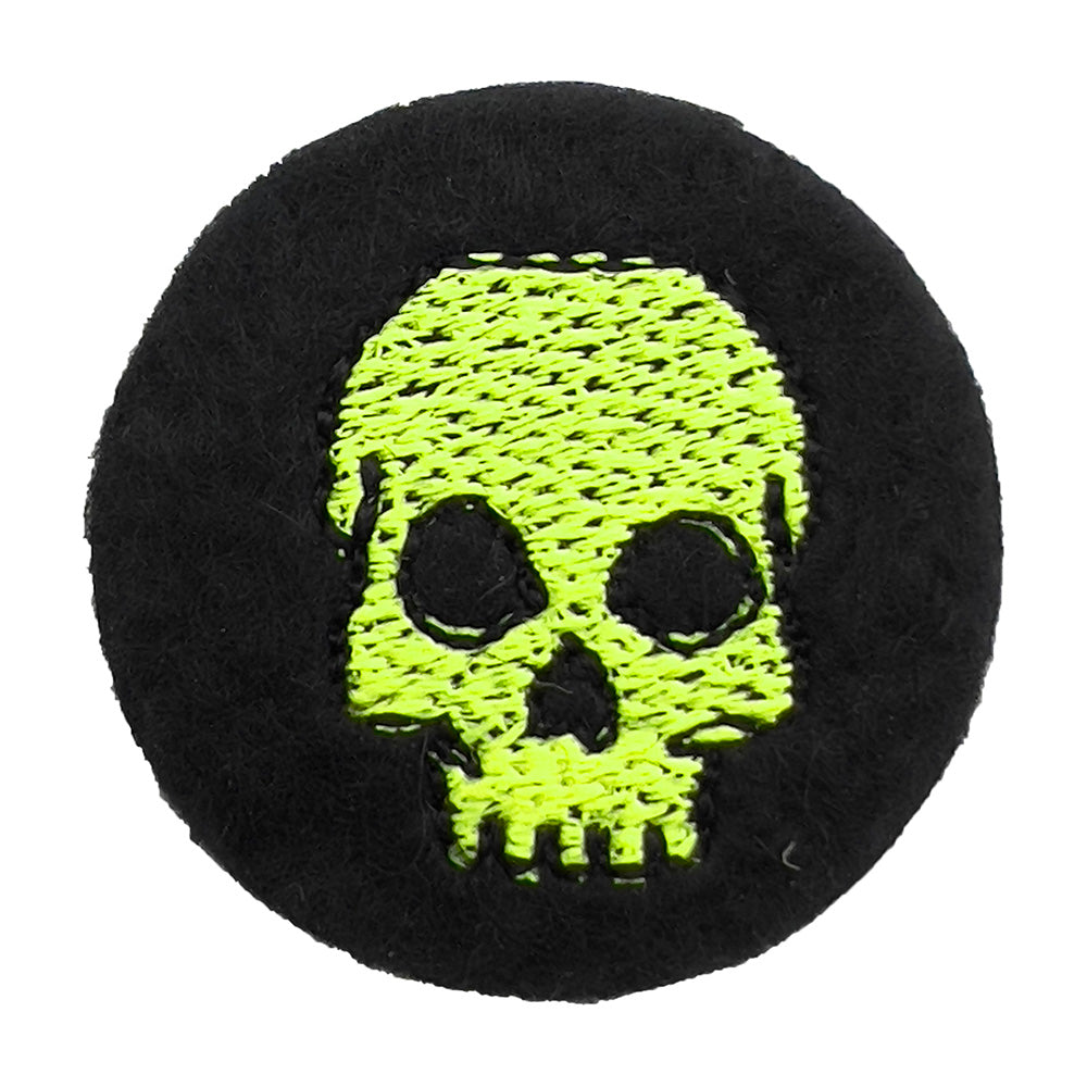 lose-up of a black felt badge featuring a yellow embroidered skull. The badge is circular and the skull design is centered with detailed stitching.