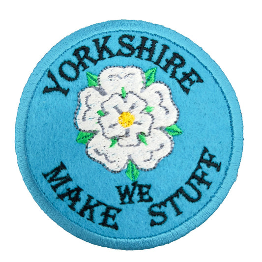 A round embroidered patch with a light blue background featuring a white rose in the center. The text "YORKSHIRE WE MAKE STUFF" encircles the rose in black stitching.