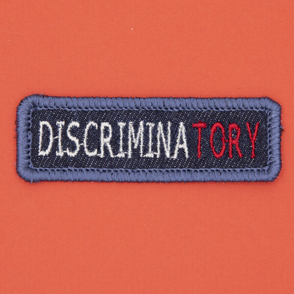 blue denim patch embroidered with the word DISCRIMINATORY