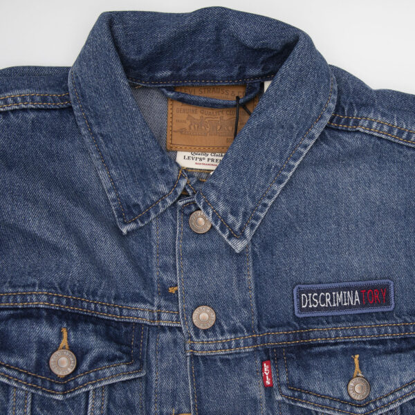demin jacket with blue denim patch embroidered with the word DISCRIMINATORY