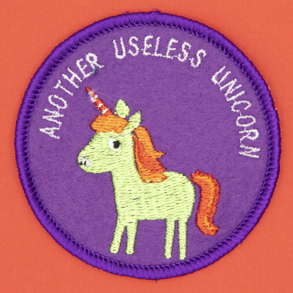 round embroidered patch picture of a green unicorn and text another useless unicorn on purple