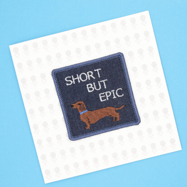 square embroidered patch picture of dachshund dog and text short but epic on blue denim