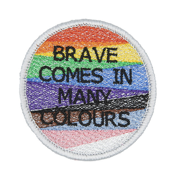 Round embroidered patch, embroidered with a silver border and pride rainbow stripes. The words BRAVE COMES IN MANY COLOURS in black text sit in top of the stripes.Photographed on a white background