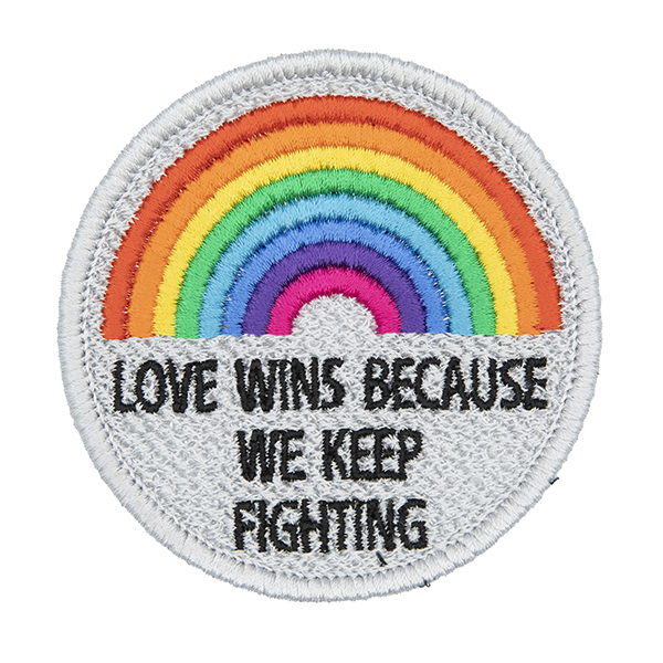 round embroidered patch, embroidered in silver with an eight colour rainbow and the words LOVE WINS BECAUSEWE KEEP FIGHTING in black text photographed ona white background