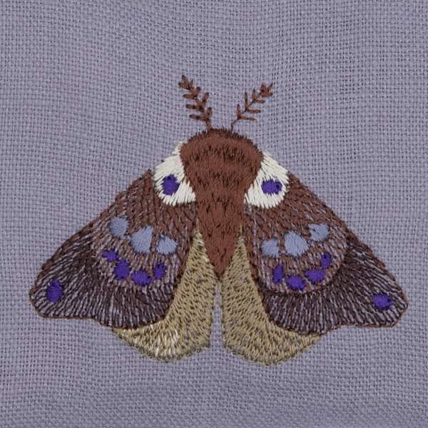 clsoe up of silver linen moth repellant bag. Embroidered moth has wings closed