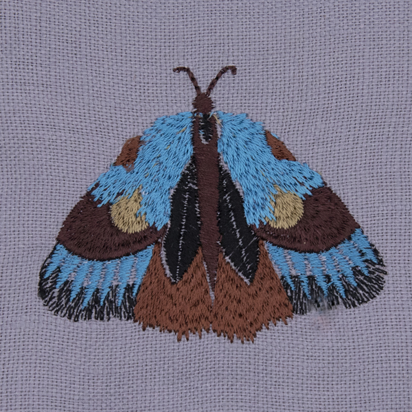 close up of silver linen moth repellant bag. Embroidered moth has wings closed
