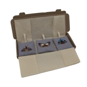 three silver linen sachets with crem hanging loops, embroidered with moths in a cardboard box with the lid open