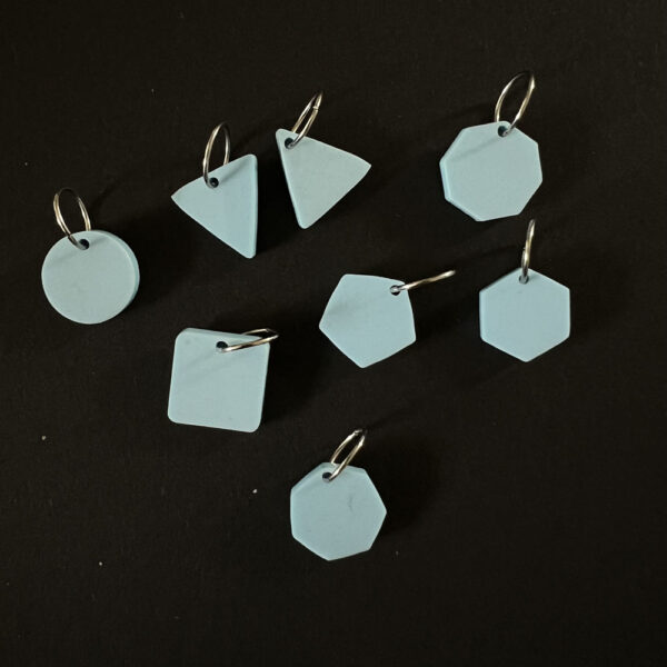 Eight geometric shapes laser cut from candy floss blue pastel perspex. Mounted jump rings to create stitch markers.