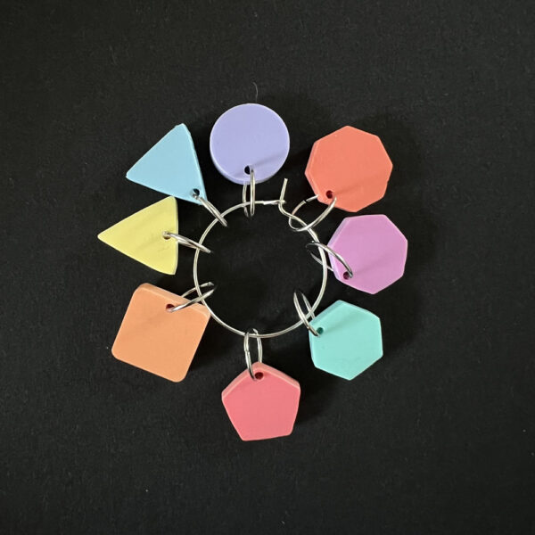 Eight geometric shapes laser cut from assorted pastel perspex. Mounted on jump rings to create stitch markers.
