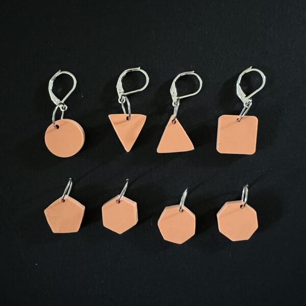 Eight geometric shapes laser cut from orange fizz pastel perspex. Mounted on a mix of jump rings and latch back hooks to create stitch markers.