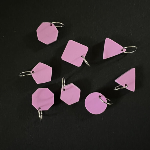 Eight geometric shapes laser cut from sour grape pink pastel perspex. Mounted on ump rings to create stitch markers.