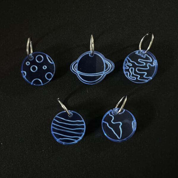 Five planets laser cut from fluorescent blue perspex, . Mounted on a jump rings to create stitch markers.