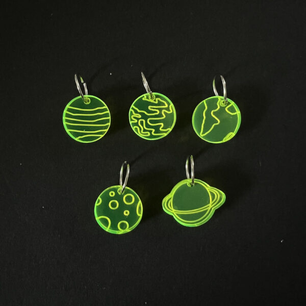 Five planets laser cut from fluorescent green perspex, . Mounted on jump rings to create stitch markers.